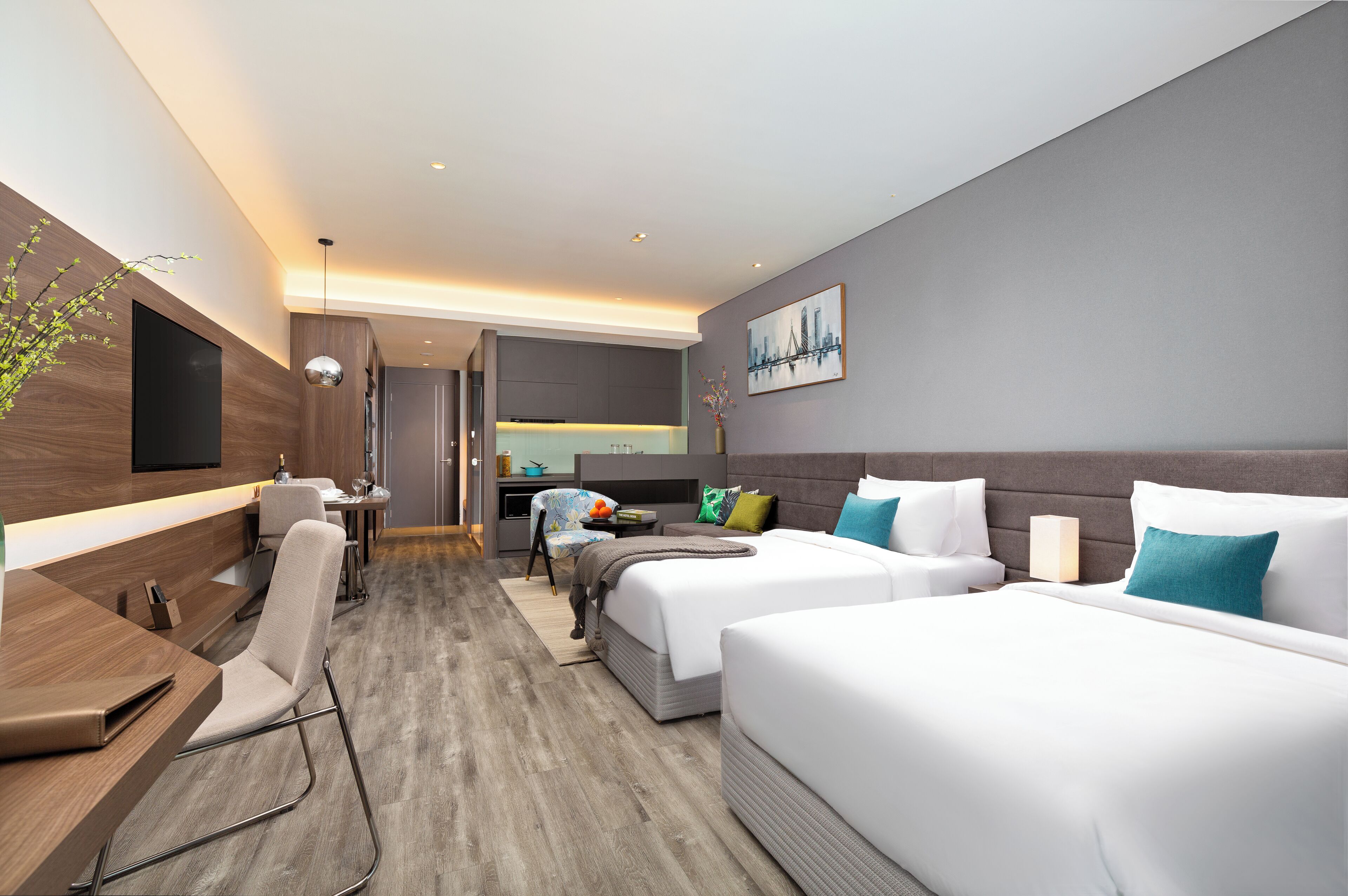 A modern hotel room with a sofa, two beds, a desk, and a TV mounted on the wall.