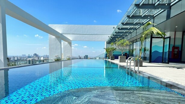 Una piscina infinita en la azotea con vistas a la ciudad, rodeada de arquitectura moderna y plantas en macetas.
