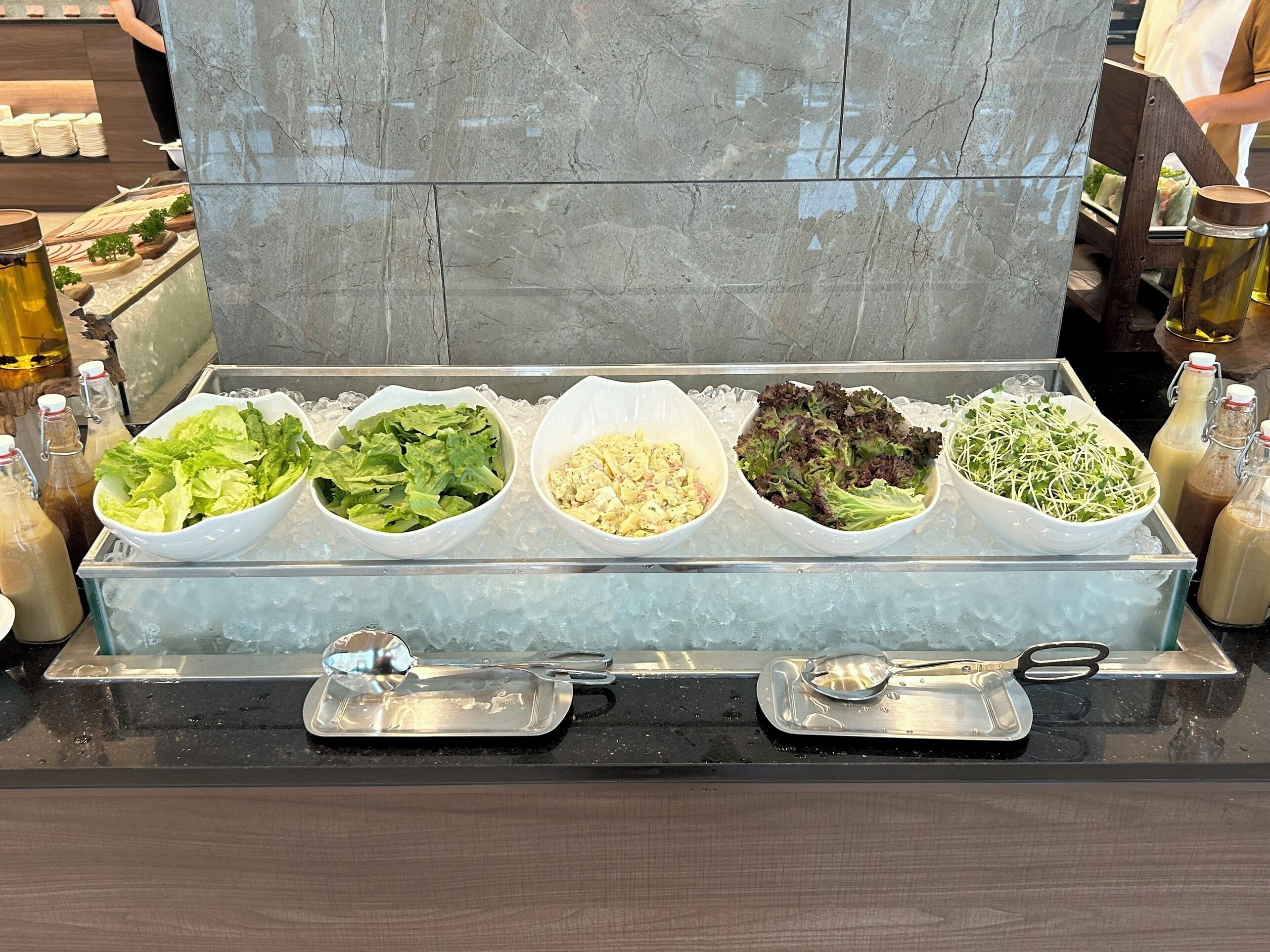 A buffet with various salads and condiments in a glass display case.