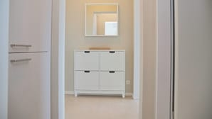 A narrow hallway with a white wardrobe and a mirror on the wall.