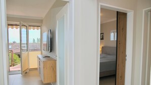 A modern apartment with a balcony, a wooden cabinet, a bed, and a TV mounted on the wall.