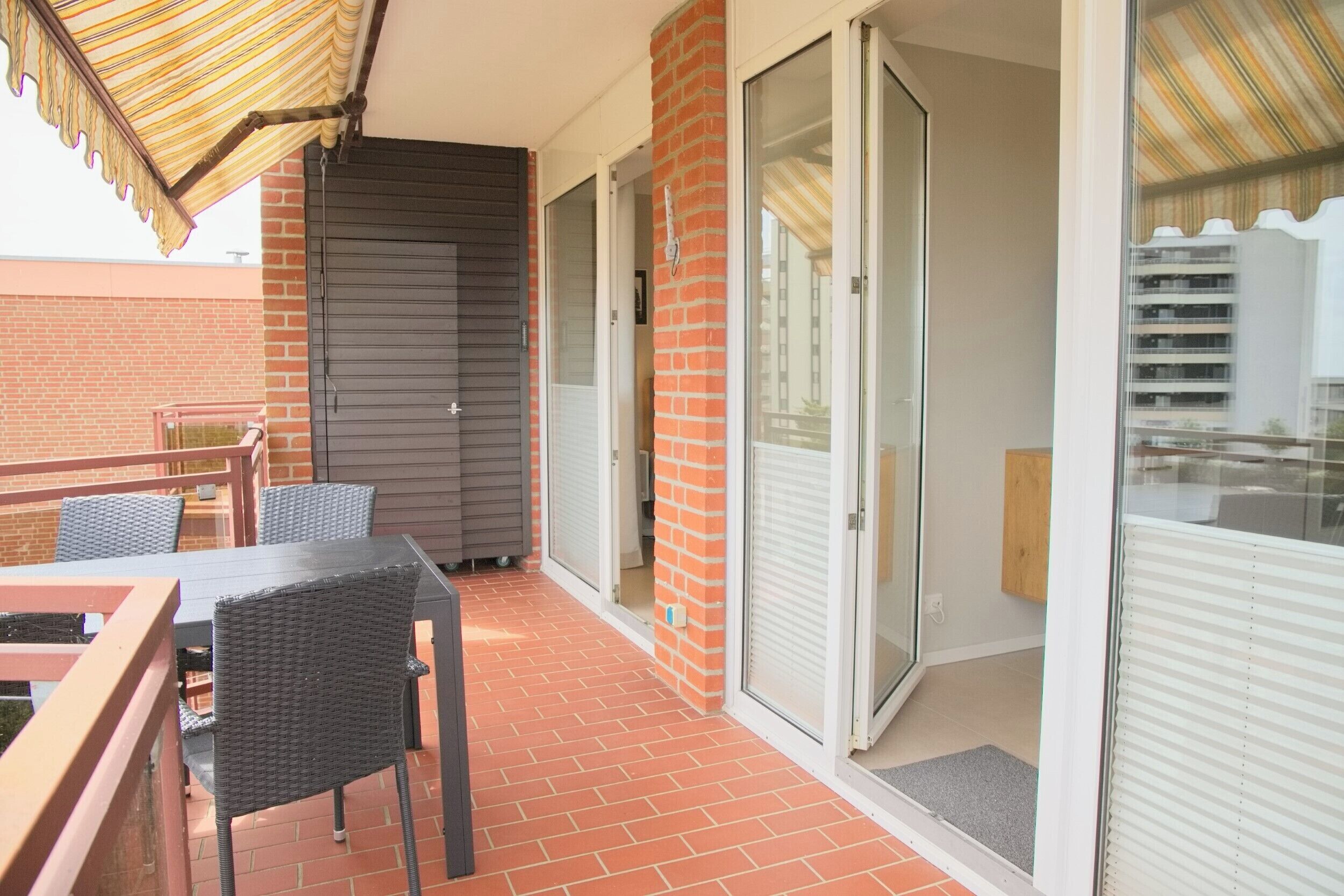 Un balcon avec une table et des chaises, une porte-fenêtre coulissante et un mur en briques.