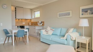 A modern living room with a light blue sofa, a dining table with chairs, a coffee machine, and a lamp on a side table.