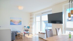 A modern living room with a sofa, a coffee table, a TV, and a dining table with chairs.