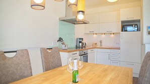 A modern kitchen with white cabinets, a wooden dining table, and pendant lighting.