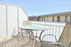 En balkon med et glasbord og stole, med udsigt over en bygning i moderne stil.
