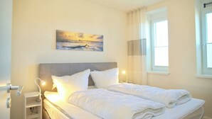 A hotel room with a bed, bedside tables, a nightstand, a painting on the wall, and a window with curtains.