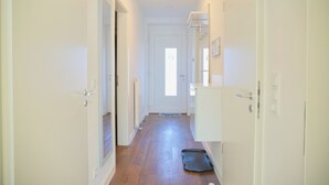 A narrow hallway with white walls and wooden flooring, leading to a door at the end.