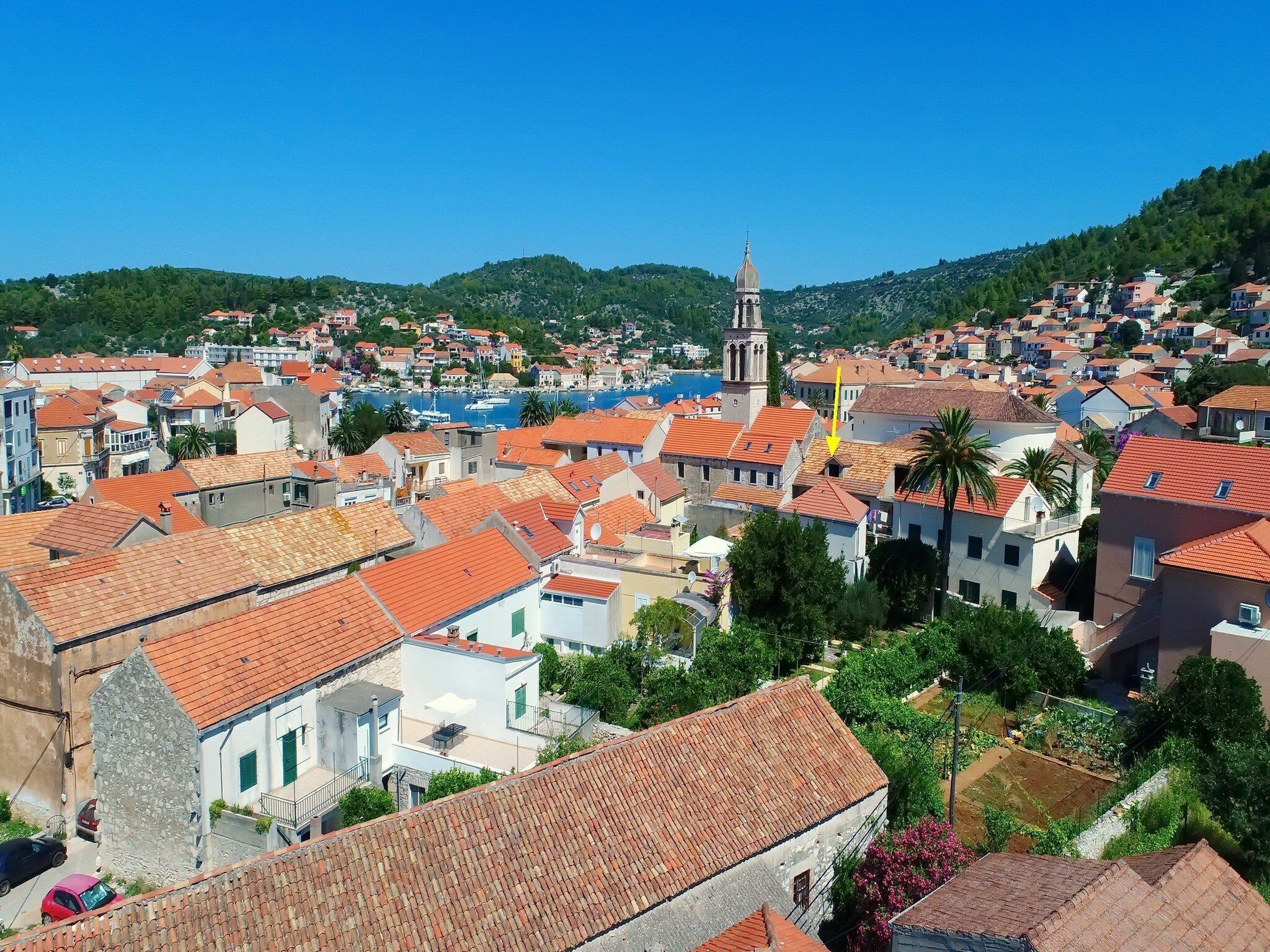 A coastal town with terracotta-roofed buildings, a prominent church tower, and a hillside backdrop.