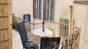 A balcony with a table and chairs, a potted plant, and a view of a building with shutters. - Studio Joković (Vela Luka)