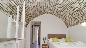 A bedroom with a stone ceiling, a bed with white bedding and green pillows, a wooden nightstand, and a white wardrobe. - Studio Joković (Vela Luka)