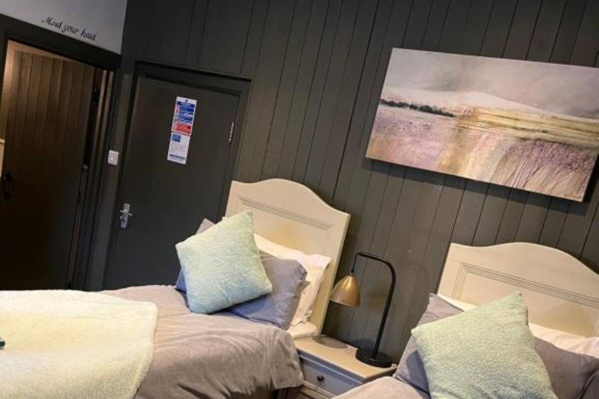 A hotel room with two beds, each with a headboard, a nightstand, and a lamp. There is a painting on the wall above the beds.