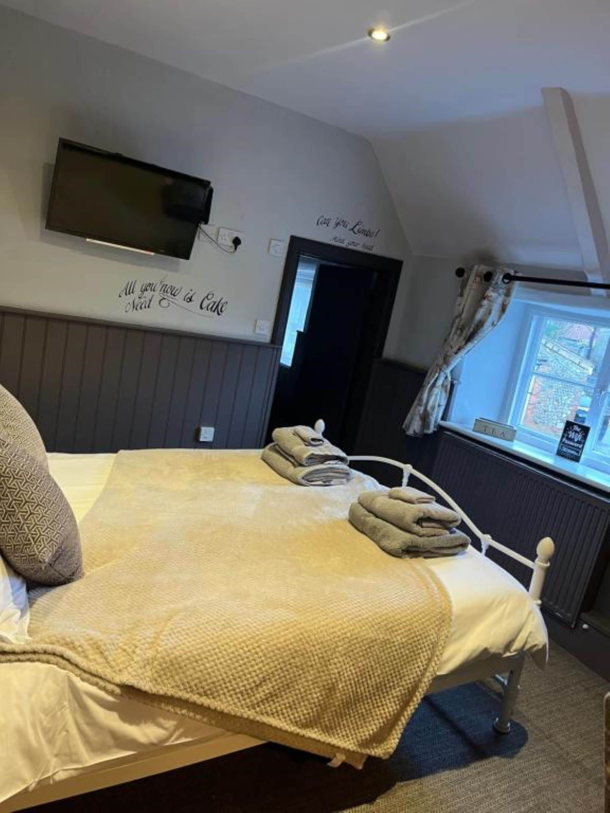 Un dormitorio con cama, televisión montada en la pared, ventana con cortinas y un letrero en la pared.