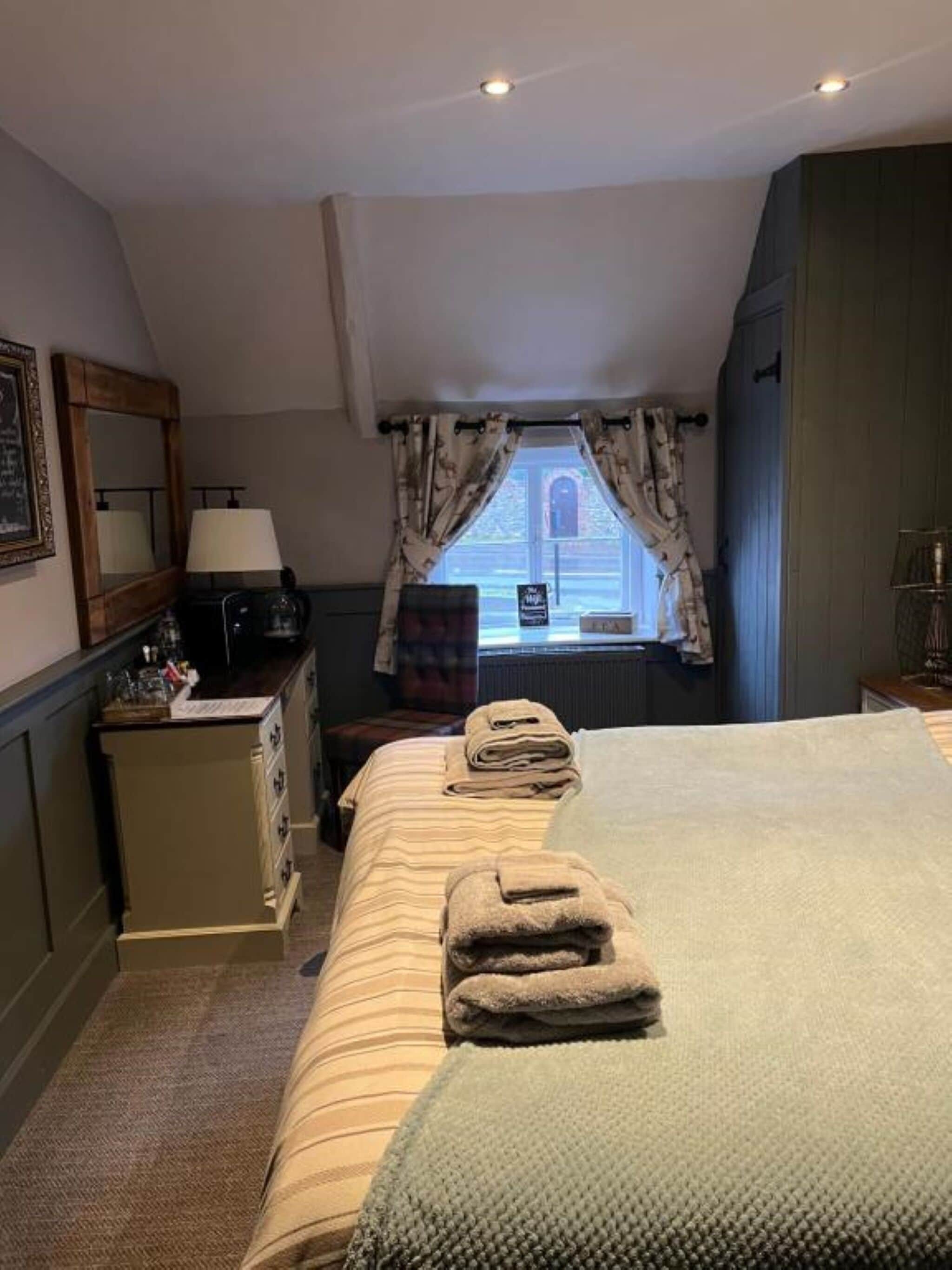A hotel room with a bed, a desk, a mirror, and a window with curtains.