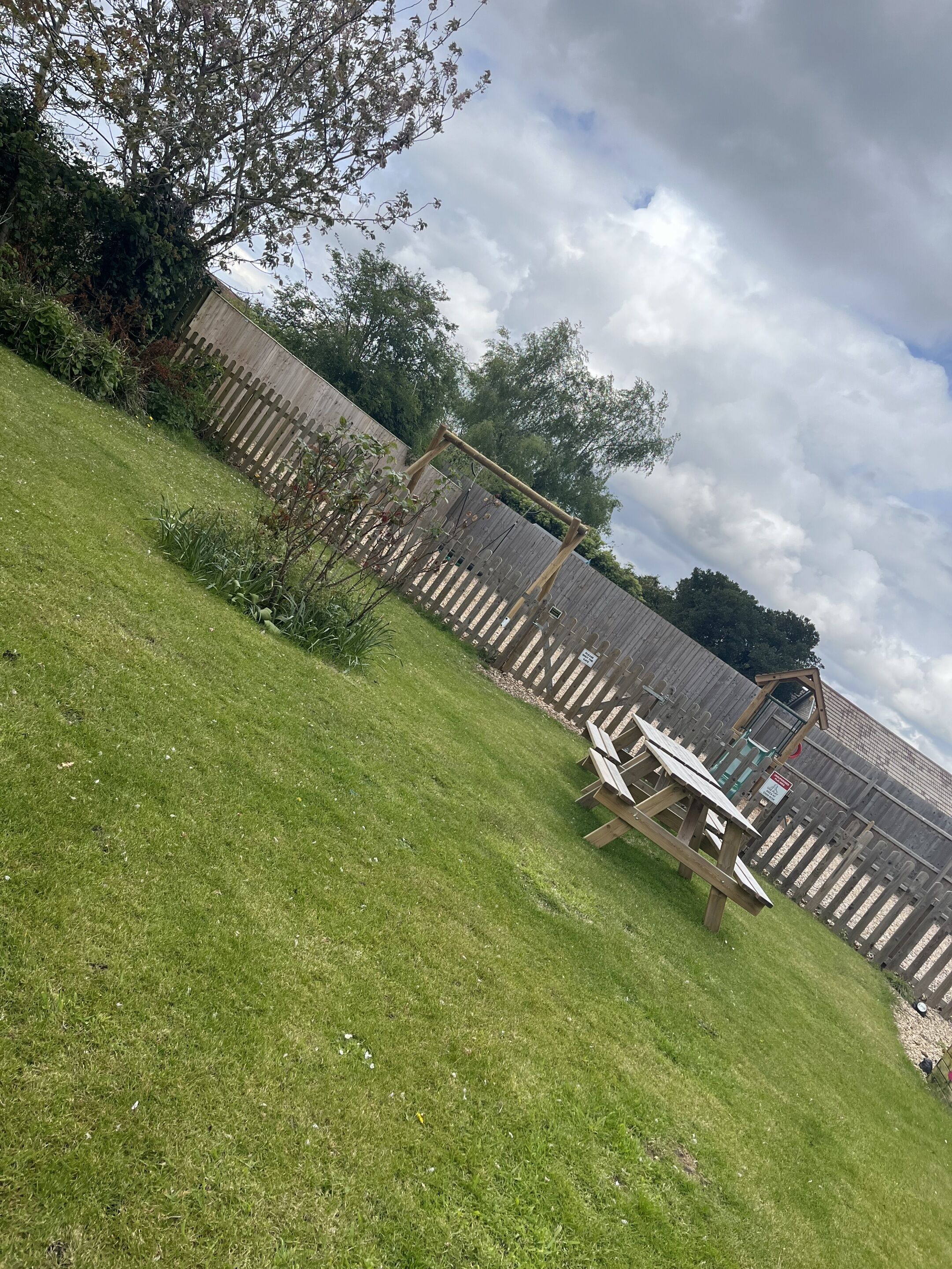 A fenced backyard with a wooden play structure, a picnic table, and a small garden area.