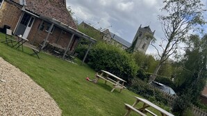 A grassy outdoor area with picnic tables, a brick building, and a stone tower in the background. - The Crown Inn (King's Lynn)