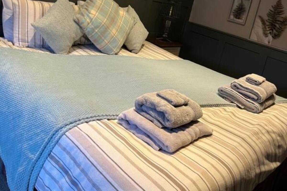 A neatly made bed with striped bedding, a headboard, and a set of folded towels on the bed.