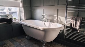 A clawfoot bathtub in a bathroom with a window, a towel rack, and a wooden floor. - The Crown Inn (King's Lynn)