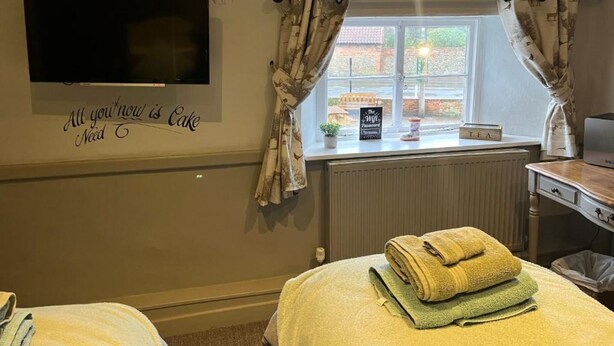 A hotel room with a bed, a TV mounted on the wall, a window with curtains, and a sign on the wall. - The Crown Inn (King's Lynn)