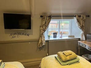 A hotel room with a bed, a TV mounted on the wall, a window with curtains, and a sign on the wall. - The Crown Inn (King's Lynn)
