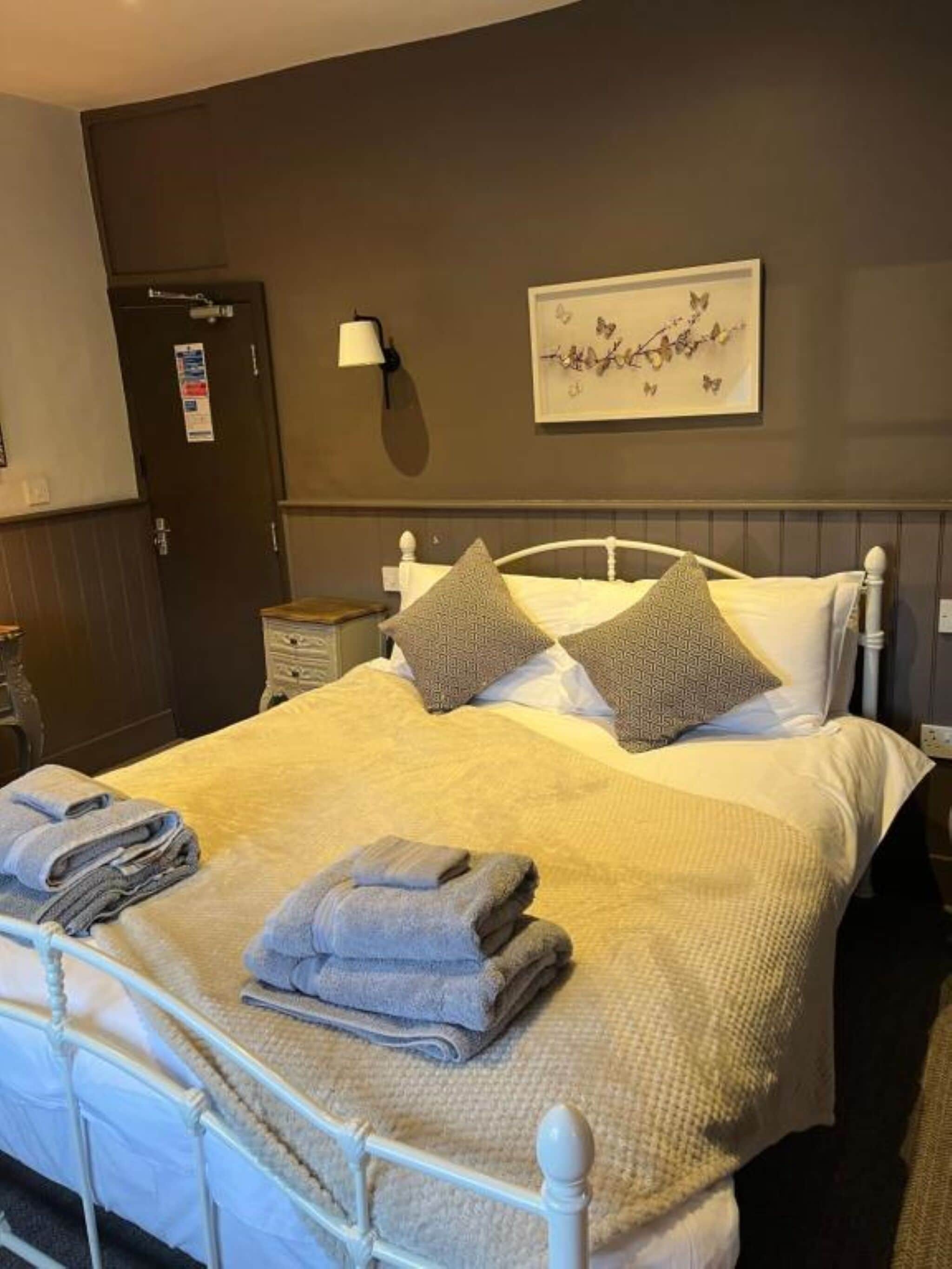 A neatly made bed with a white headboard, two pillows, and folded towels on the side.