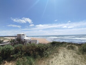 A coastal view with a white building, sandy beach, and ocean waves.