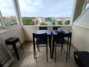 A balcony with a table and chairs, a view of buildings and trees, and a tiled floor.