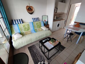 A living room with a sofa, a coffee table, a dining table, and a washing machine in the background.