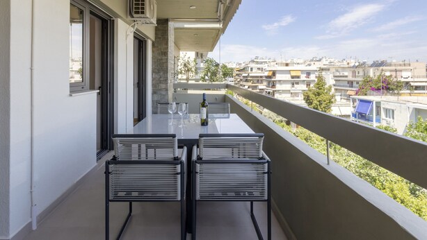 En balkon med et bord og stole, en flaske vin og udsigt over bybilledet.