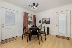 Un coin repas avec une table ronde, quatre chaises, un ventilateur de plafond et un tableau accroché au mur.