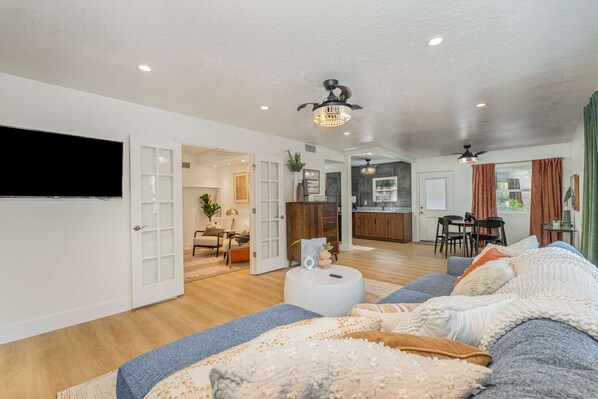 A spacious living room with a large sofa, a dining area with a table and chairs, a kitchen with dark cabinets, and a ceiling fan.