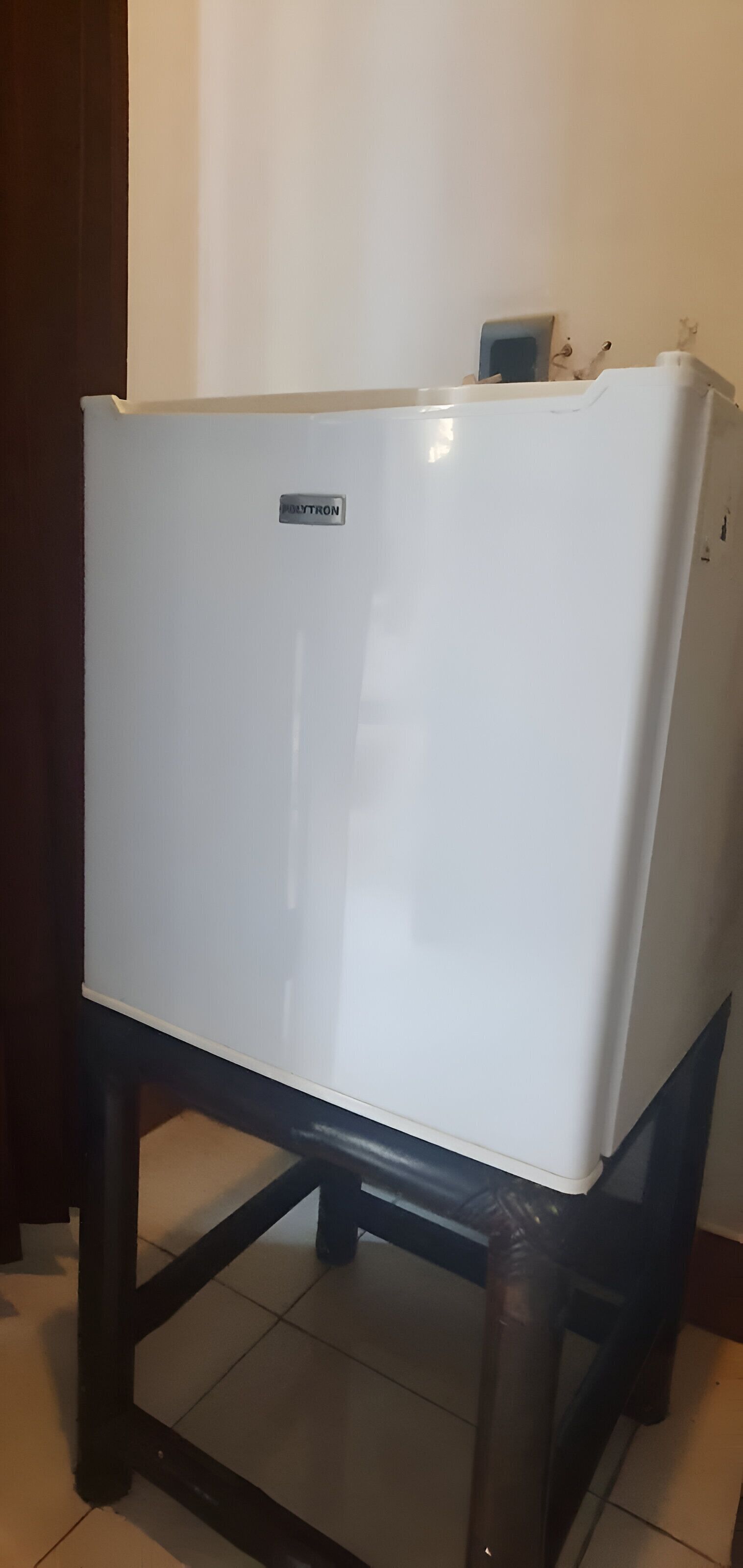 A white refrigerator on a black metal stand in a room with tiled flooring.