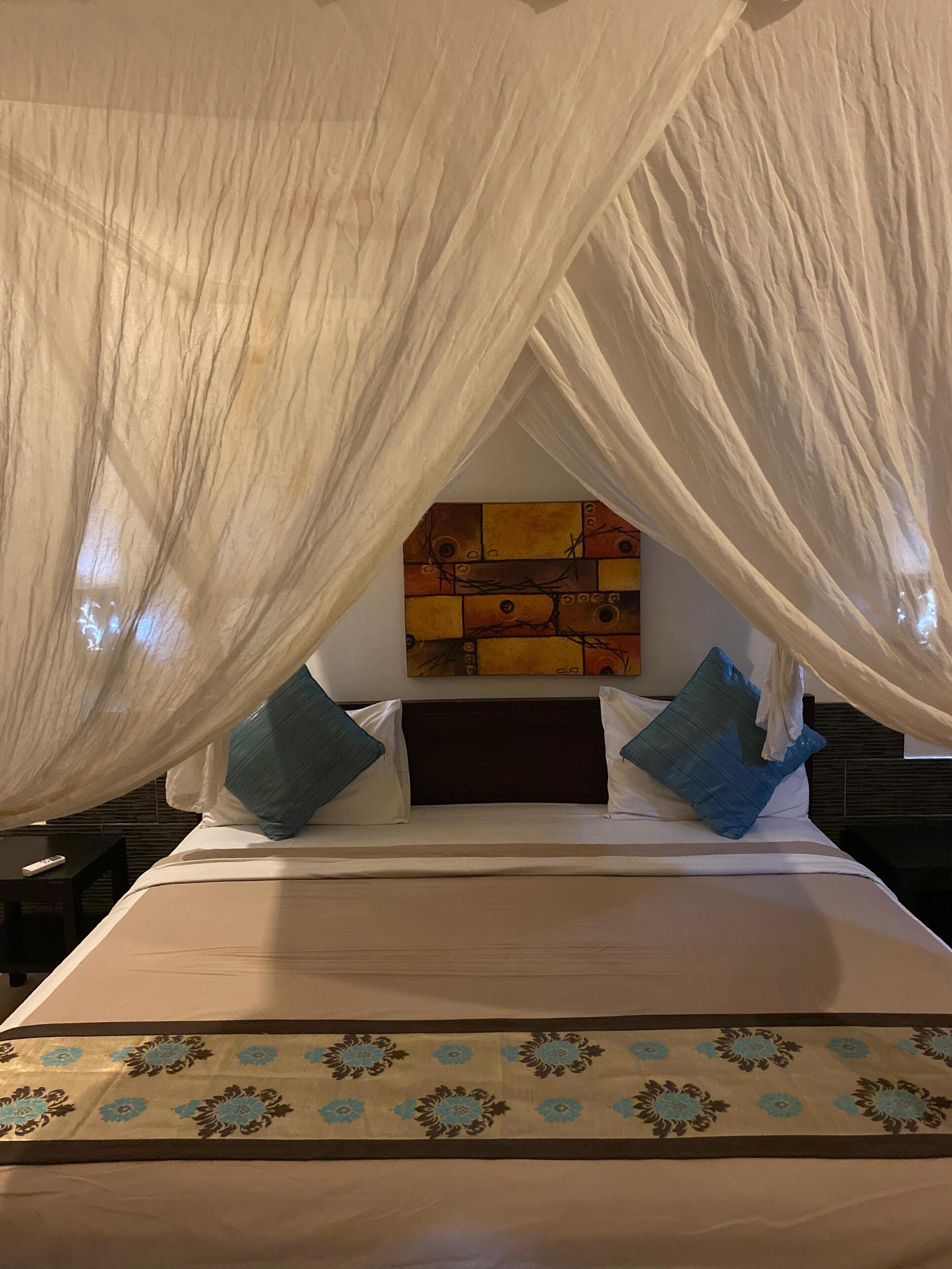 A bed with a canopy, a headboard with a colorful painting, and a patterned bedspread.