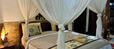 A four-poster canopy bed with a floral bedspread, a bedside table with a lamp, and a view of the outdoors.