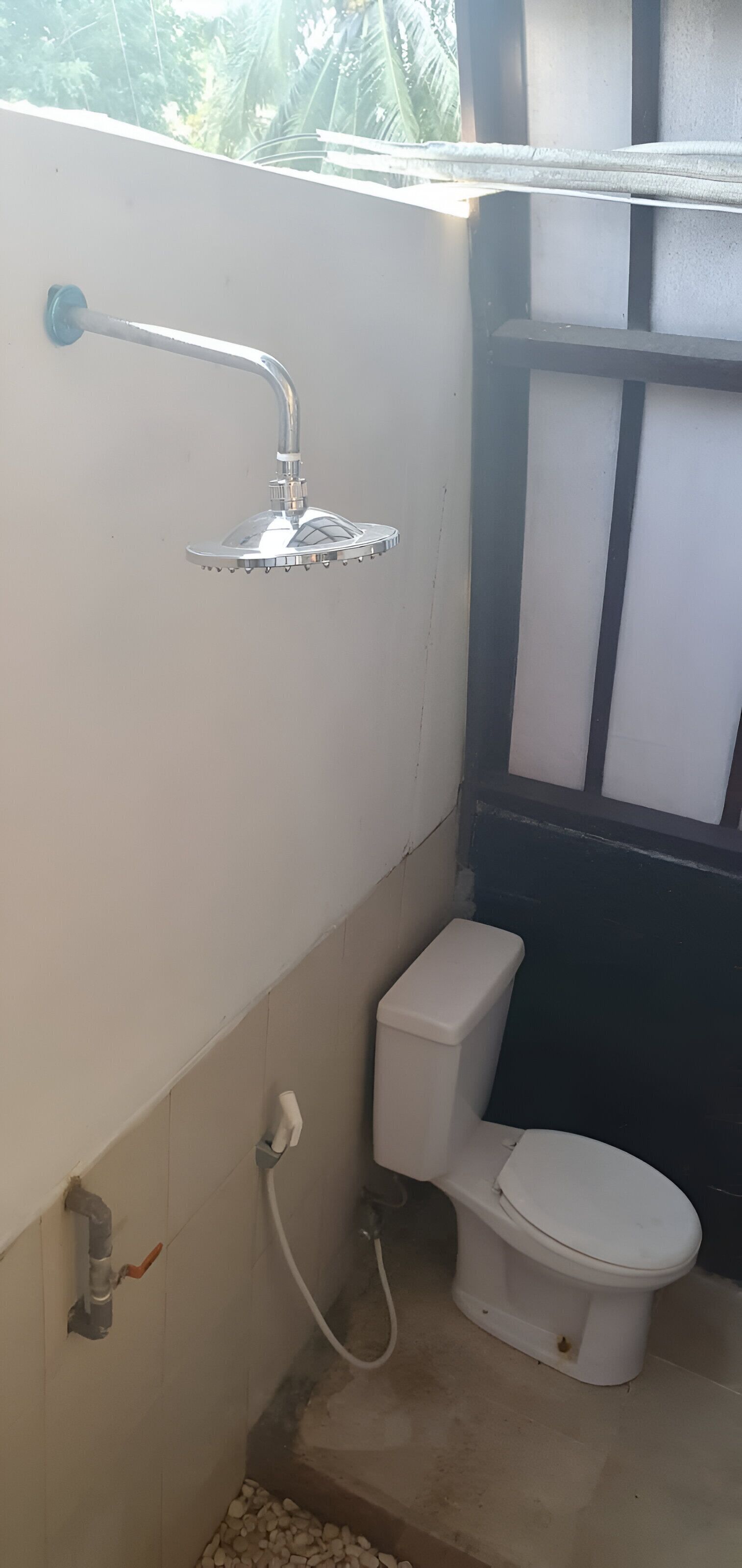 A small bathroom with a shower, toilet, and a window with blinds.