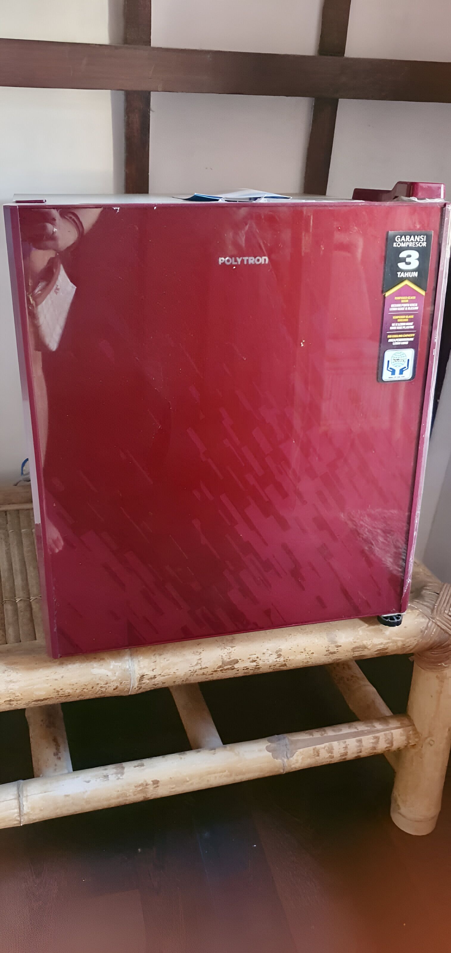 Un réfrigérateur rouge posé sur un tabouret en bois.