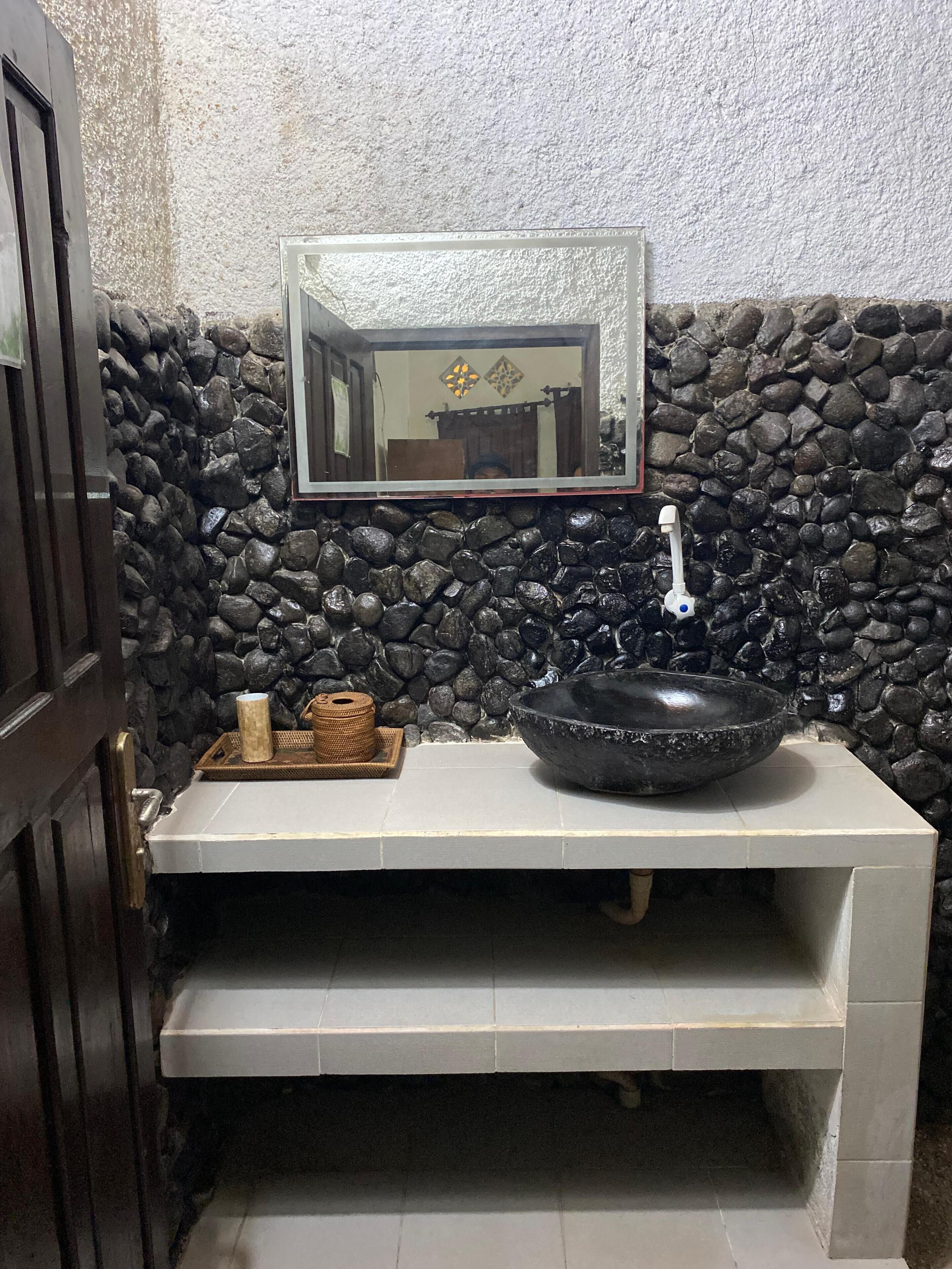 A bathroom with a stone wall, a sink with a black basin, and a mirror above it.