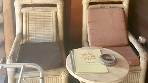 Dos sillones de mimbre con cojines, una mesita redonda con un menú, y una silla de metal con respaldo.