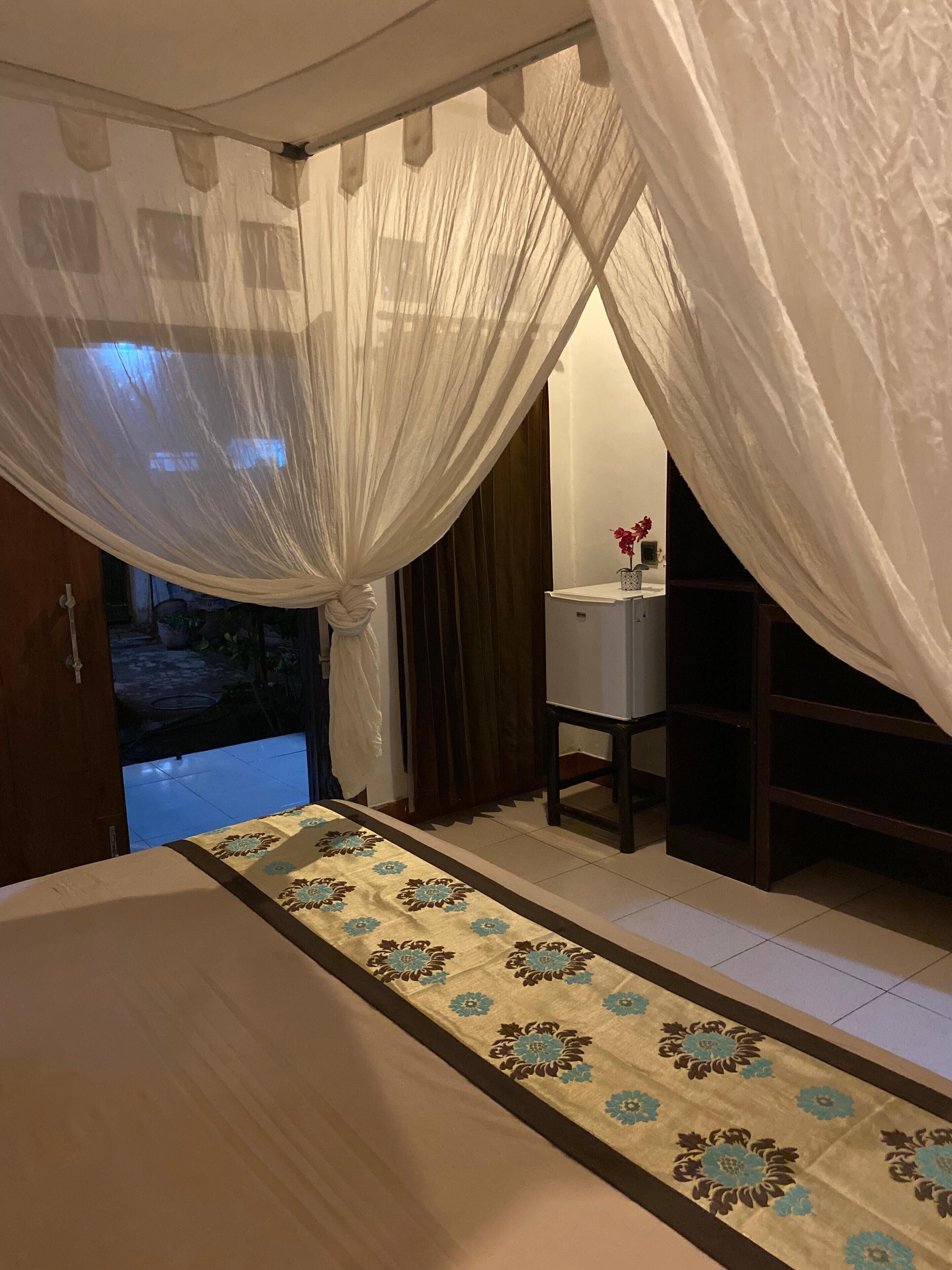 A bedroom with a bed, a bedside table, a mirror, and a window with curtains.