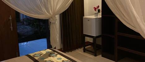 A bedroom with a bed, a bedside table, a mirror, and a window with curtains.