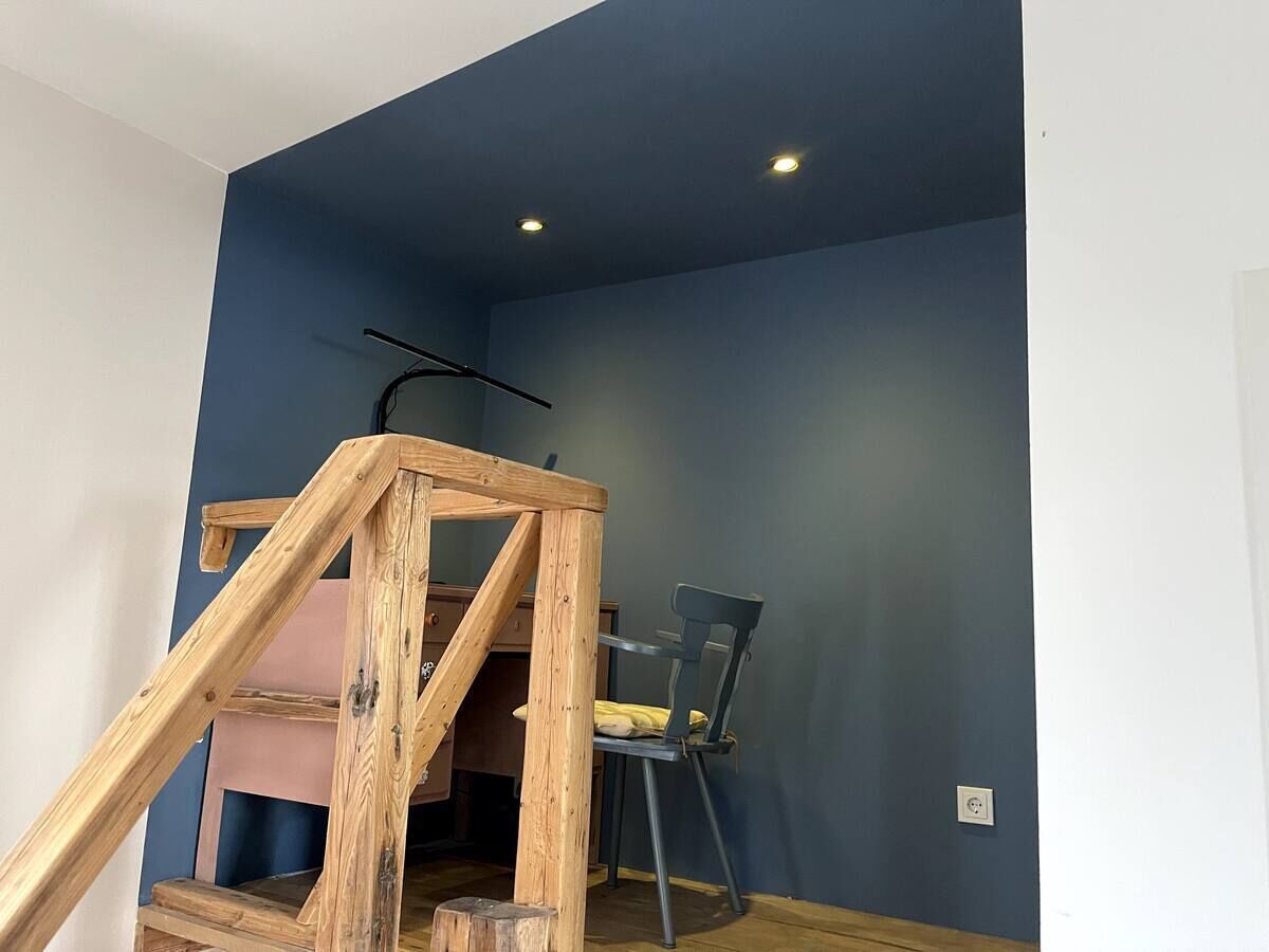 Una habitación con pared azul, una silla de madera y una estructura de madera en construcción.