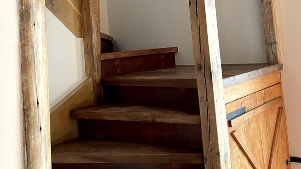 A wooden staircase with a rustic design, leading to a landing with a white wall and a radiator. - Complete apartment, 4 sleeping areas for up to 8 people (Bielefeld)