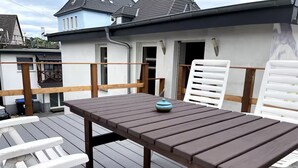 A wooden deck with a table and white chairs, overlooking a residential area with houses and a clear sky. - Complete apartment, 4 sleeping areas for up to 8 people (Bielefeld)