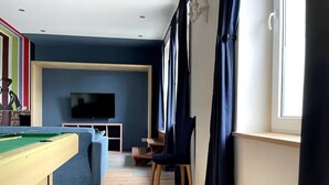 A living room with a pool table, a sofa, a TV, and a window with curtains. - Complete apartment, 4 sleeping areas for up to 8 people (Bielefeld)