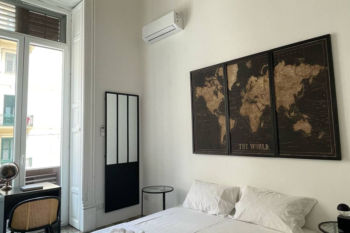 A hotel room with a large bed, a world map artwork, a standing mirror, and a small round table.