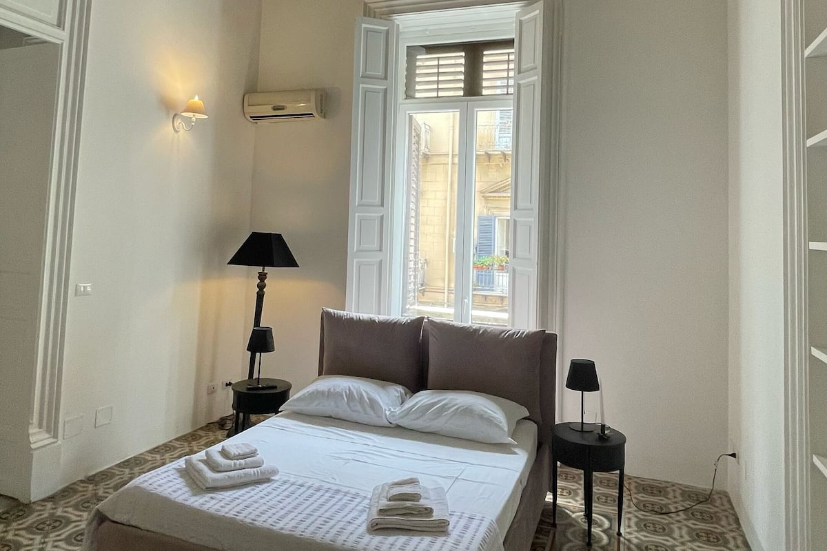 A bedroom with a large bed, a window, patterned floor, and a decorative ceiling.