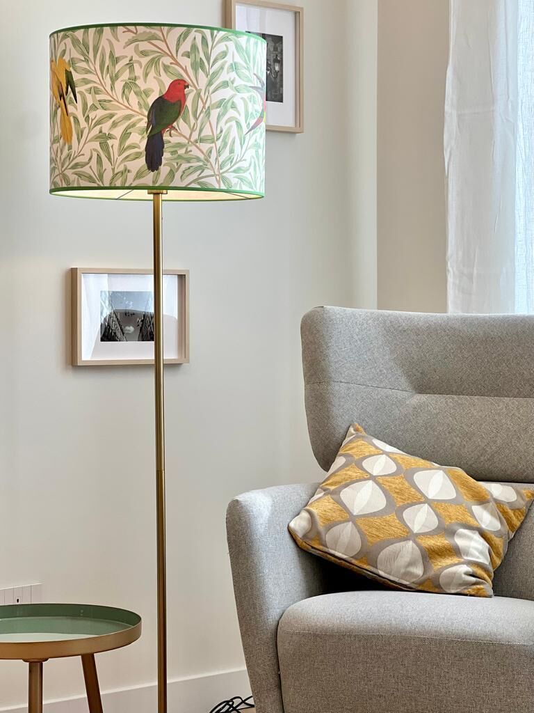Una habitación con un sillón gris, una lámpara de pie con estampado, una mesita redonda y cuadros en la pared.