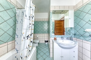 Bathroom features a green-tiled floor and walls with a playful penguin pattern on the shower curtain, a toilet, sink, and mirror.