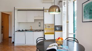 Una cocina moderna con armarios blancos, una estufa negra y una encimera amarilla. Hay una mesa de comedor con sillas y una cesta de fruta.