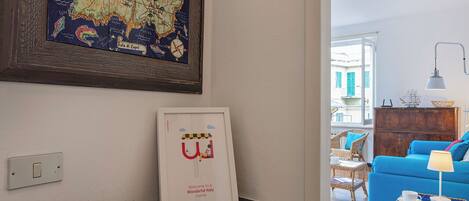 A living room with a framed map, a framed welcome sign, a wooden cutting board, and a wicker side table.